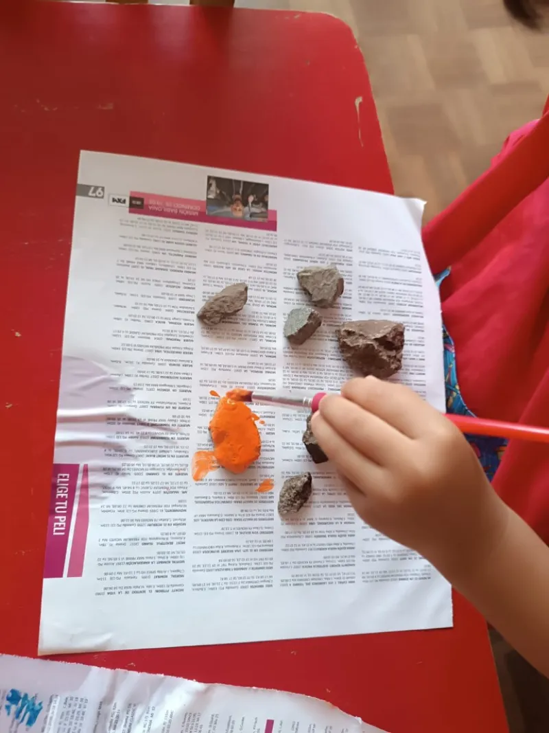 Niño pintando piedra con pincel y témpera naranja en taller de arte Años Mágicos